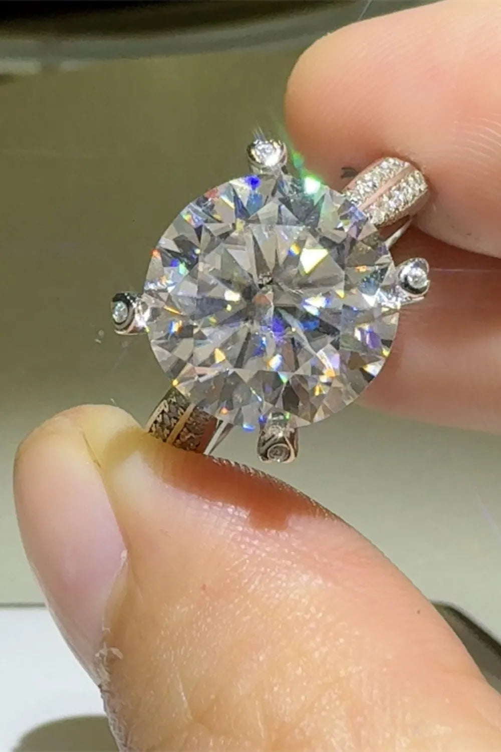 Stunning 5 carat moissanite ring held by a finger, featuring a brilliant round cut and intricate band design