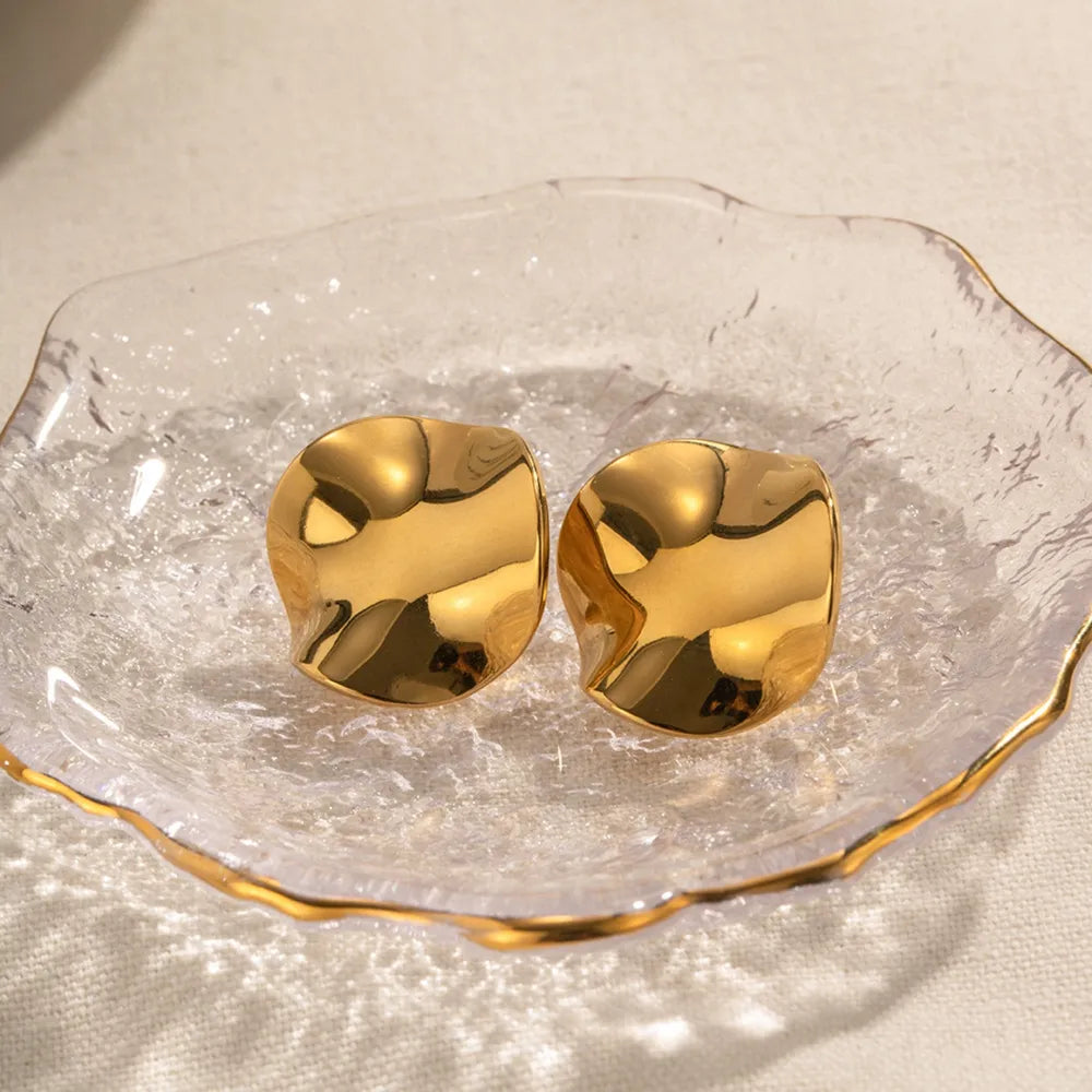 Trendsi modern gold stud earrings displayed on a crystal dish with a reflective surface