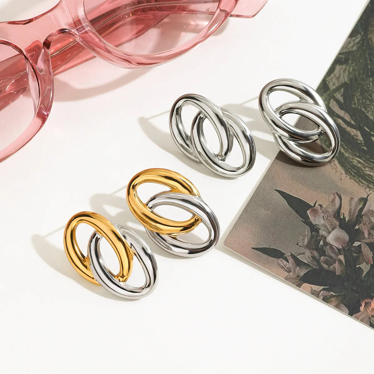 Trendy modern twist hoop earrings in silver and gold displayed with pink sunglasses