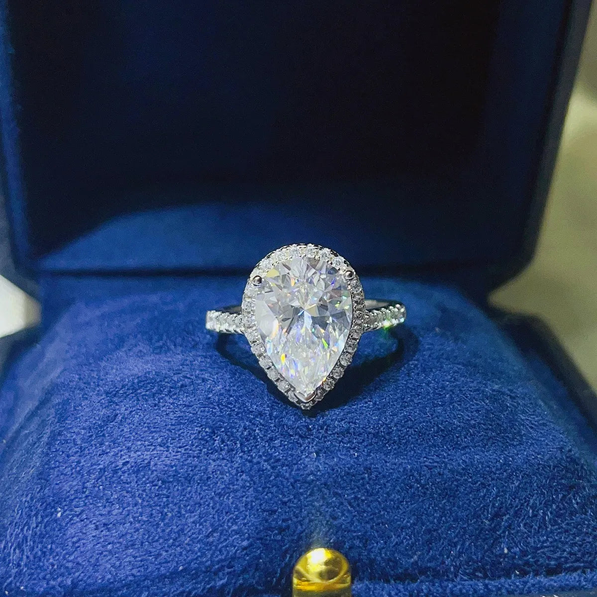 Elegant pear shaped moissanite ring with halo setting, showcased in a blue velvet box