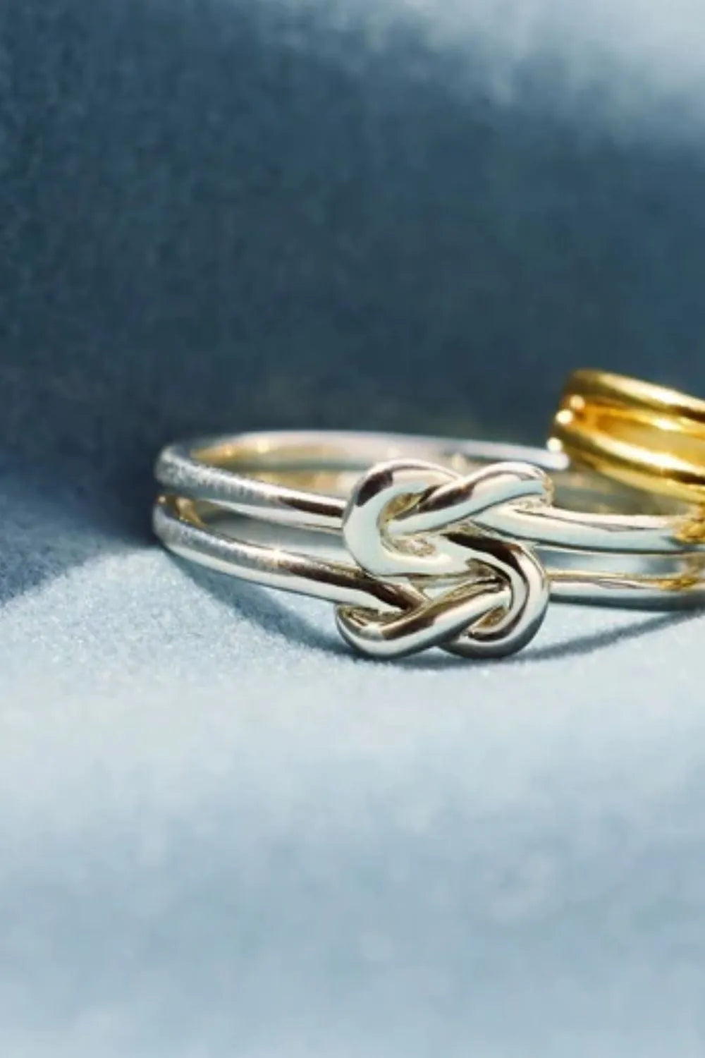 Trendsi silver knot design ring featuring an intricate intertwined pattern on a soft blue background