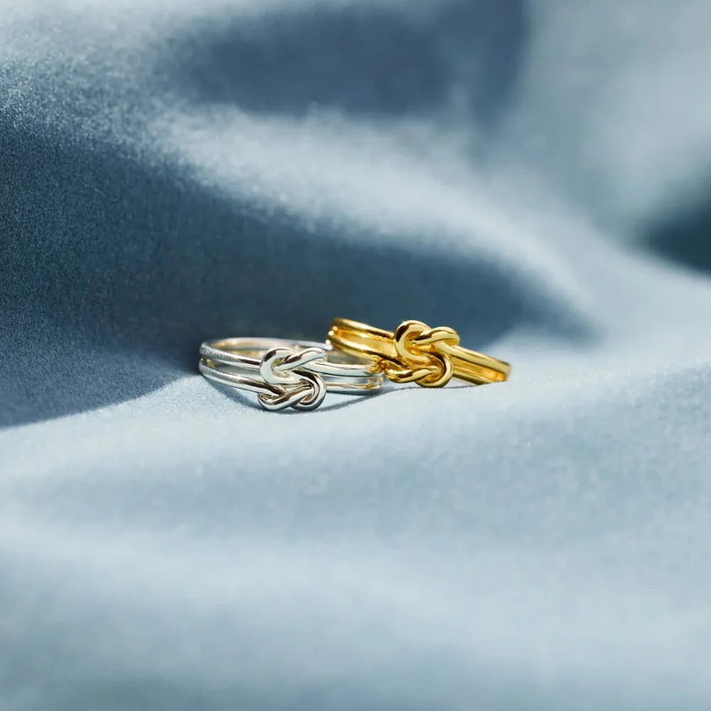 Silver knot design ring paired with a gold knot design ring on soft fabric background