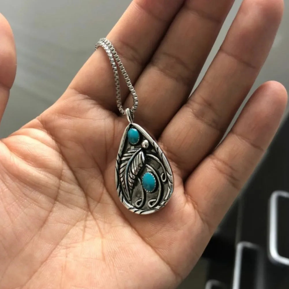 Hand holding a silver teardrop turquoise necklace for women with intricate design and turquoise stones