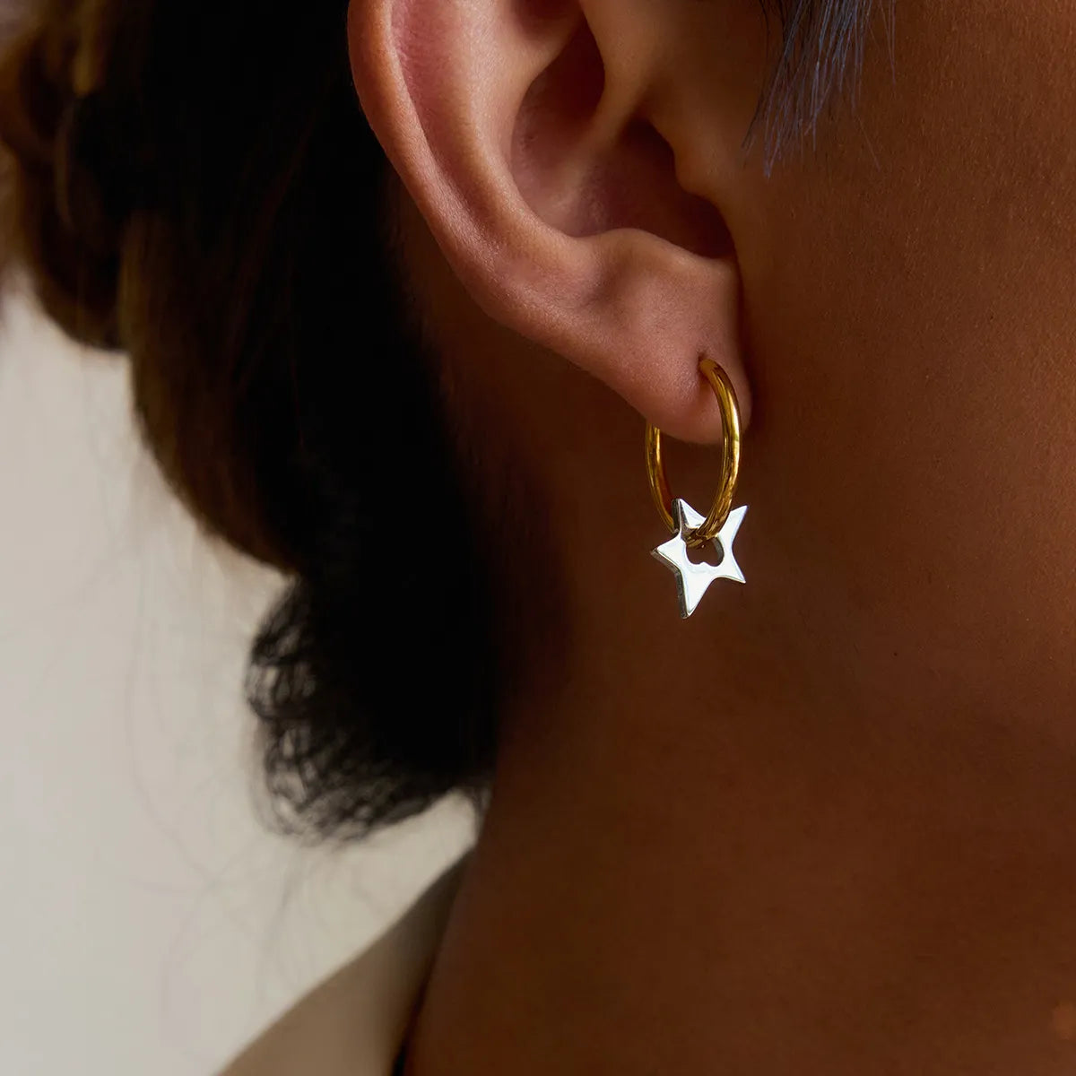 Stylish two-tone star hoop earrings hanging from an ear for a trendy look