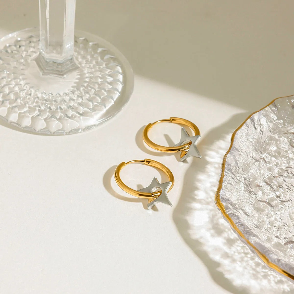 Trendsi two-tone star hoop earrings set on a stylish table with glassware and dish.