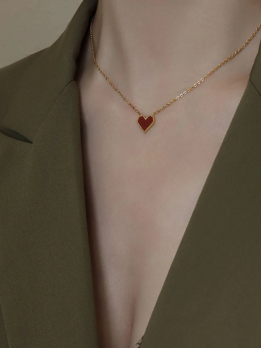 Elegant heart jewelry necklace with a gold chain and a red heart pendant on a stylish blazer