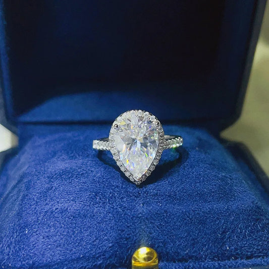 Elegant pear shaped moissanite ring with halo setting, showcased in a blue velvet box