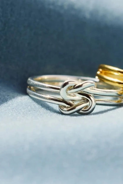 Trendsi silver knot design ring featuring an intricate intertwined pattern on a soft blue background